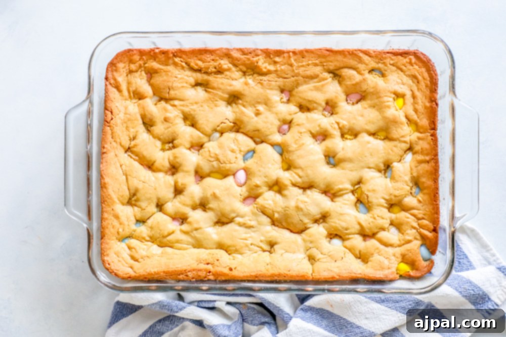 Gooey Easter blondies with colorful Cadbury Mini Eggs in a glass dish on a blue and white striped cloth, showing their delicious texture.