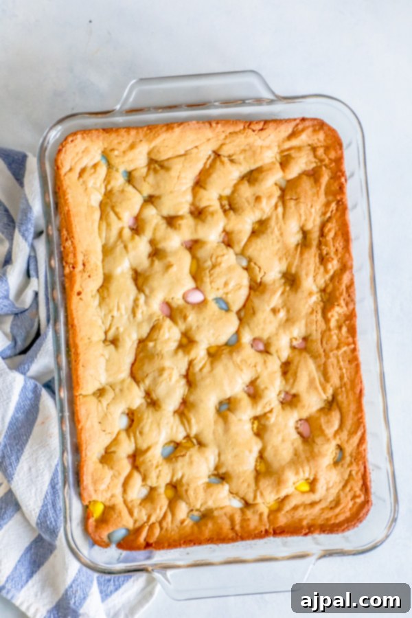 Close-up of golden Cadbury Mini Egg Blondies, featuring their irresistibly gooey texture and colorful candy pieces, served in a clear glass baking dish.