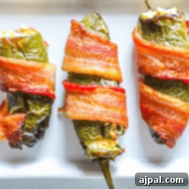 Three bacon-wrapped cheddar and garlic jalapeño poppers filled with cheese sit on a white plate, offering an easy low-carb treat perfect for keto enthusiasts.