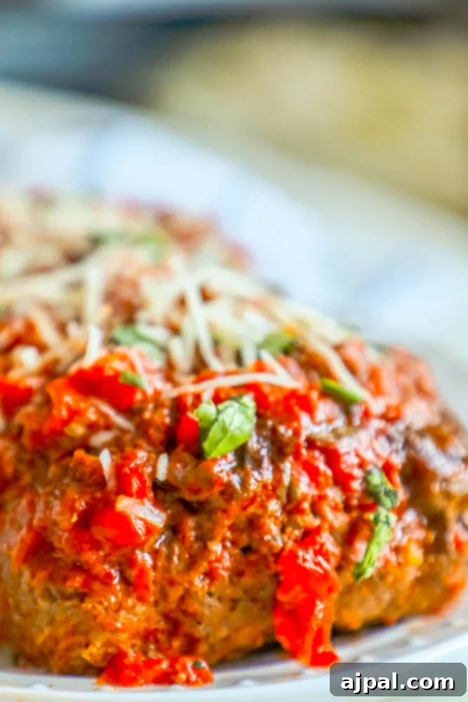 A close-up of a perfectly baked Italian meatloaf slice, glistening with marinara sauce and sprinkled with fresh Parmesan cheese, showcasing its moist texture and rich, savory appeal as a gluten-free and low-carb option.