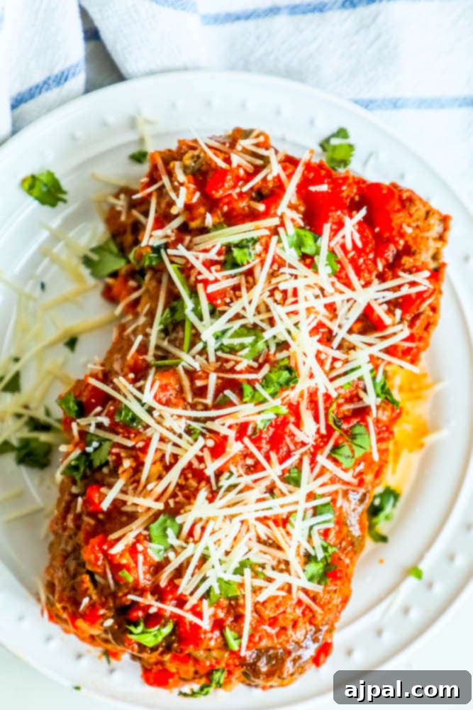 A savory slice of keto-friendly Italian meatloaf topped with juicy tomatoes and rich Parmesan, emphasizing its healthy and delicious qualities.