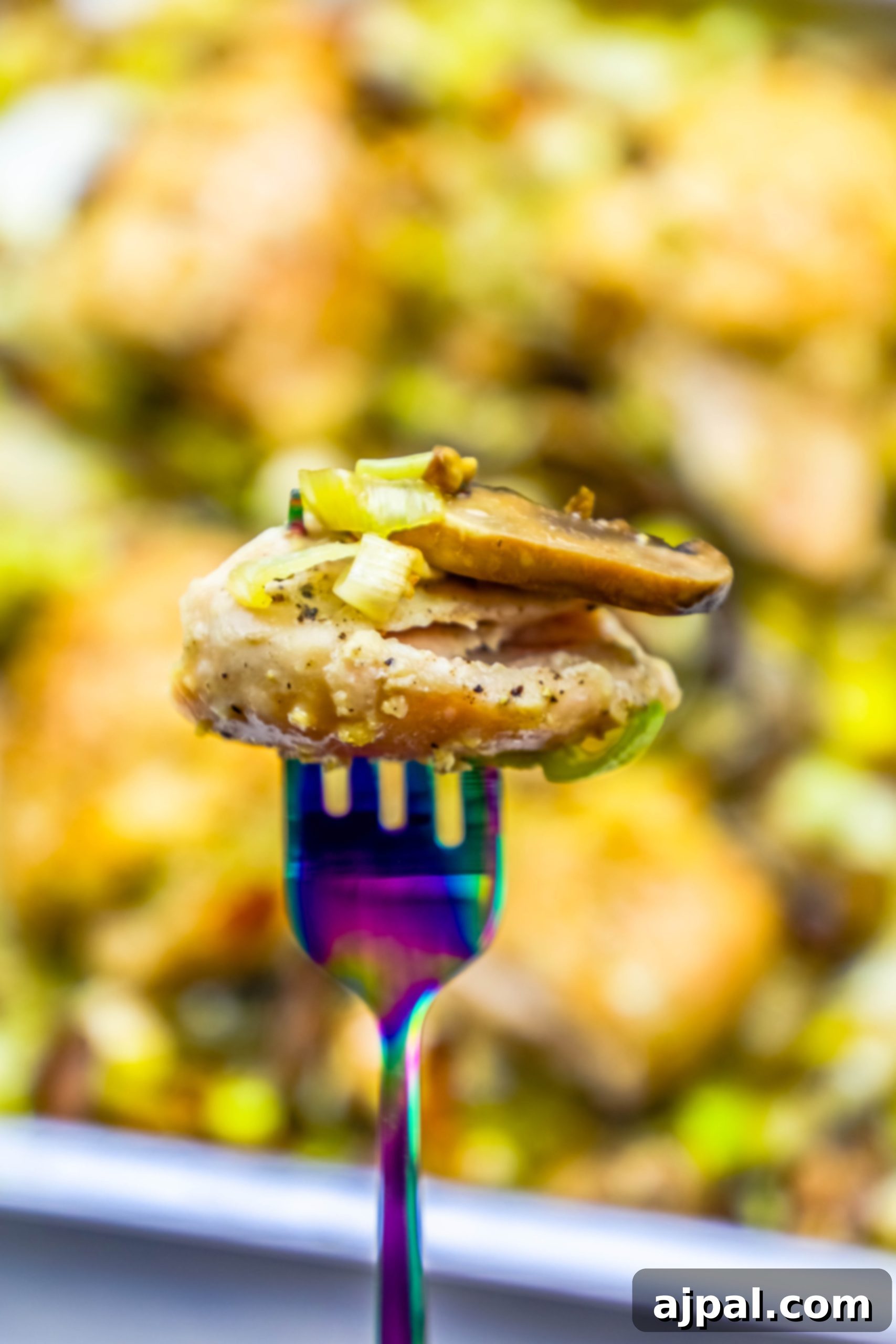 Sheetpan oven roasted chicken and leeks dinner recipe A fork holding a piece of perfectly roasted chicken, with a blurred background of the sheet pan chicken and leeks dish.