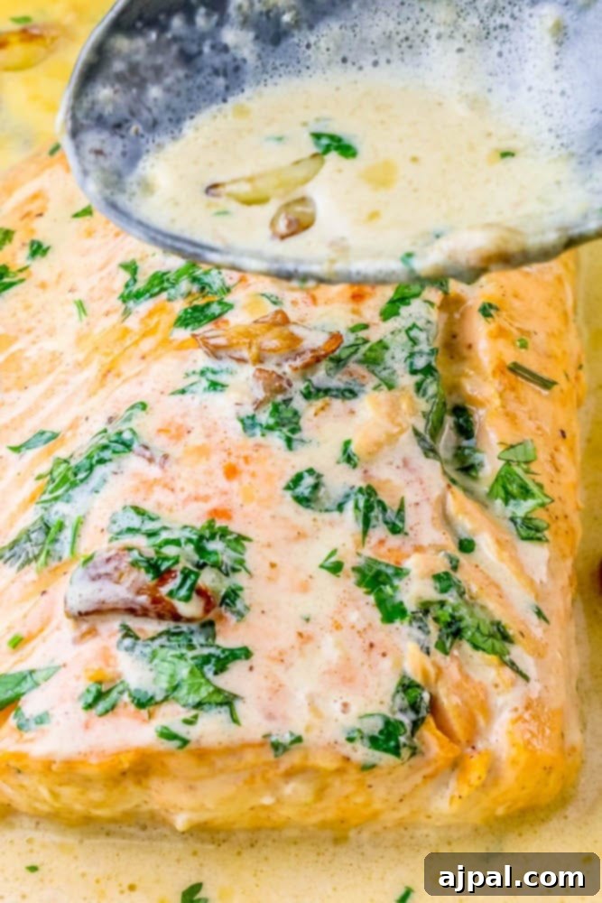 a spoon drizzling whiskey cream sauce over salmon topped with chopped parsley and garlic cloves