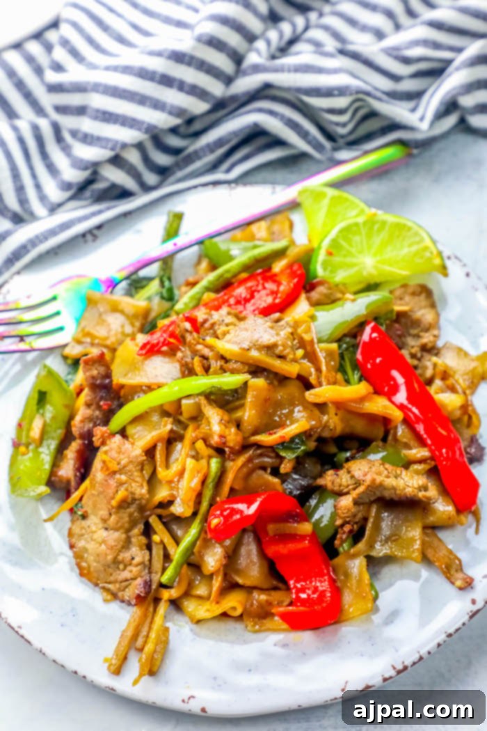 Effortless One Pot Beef Drunken Noodles 7 A hearty portion of Beef Drunken Noodles, artfully arranged on a rustic plate, brimming with tender beef, colorful vegetables, and wide rice noodles coated in a rich, savory sauce.