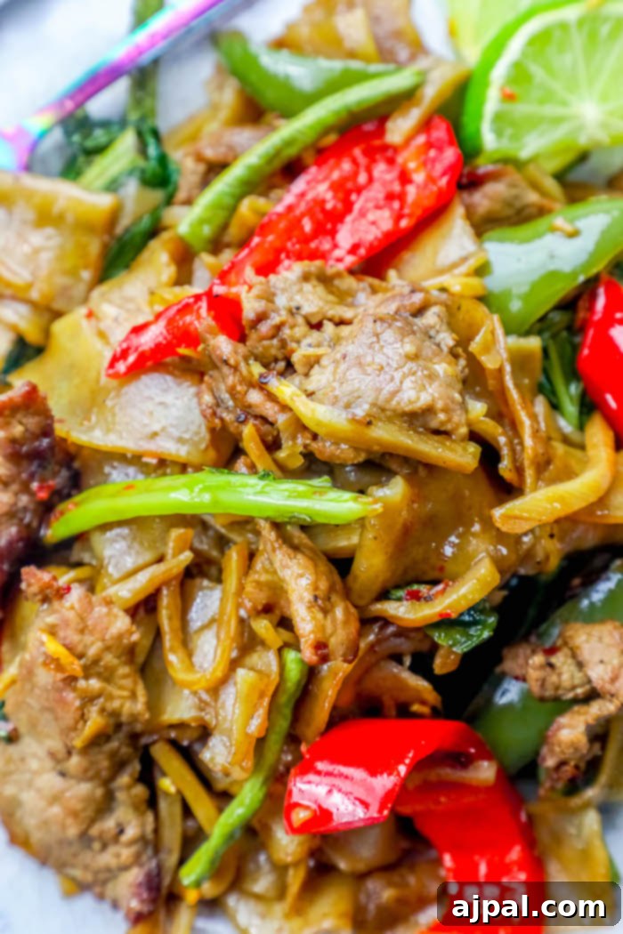 Effortless One Pot Beef Drunken Noodles 4 A delectable close-up of Beef Drunken Noodles in a pristine white bowl, showcasing the rich sauce coating the wide noodles, tender beef, and colorful vegetables.