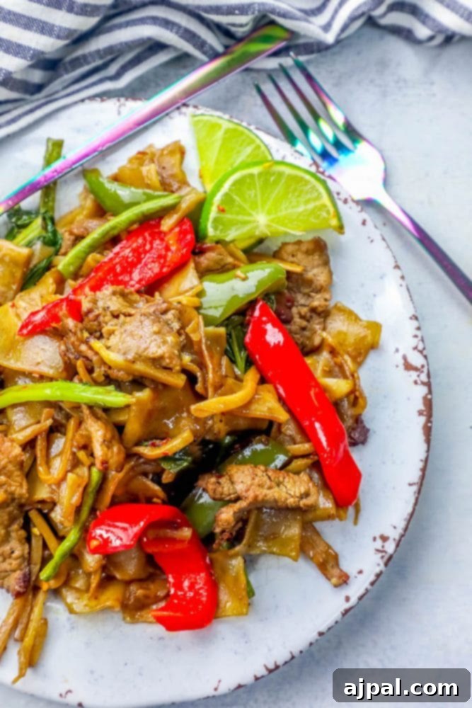 Effortless One Pot Beef Drunken Noodles 5 An appetizing serving of Thai Beef Drunken Noodles arranged on a white plate, garnished with fresh herbs and sliced chilis.