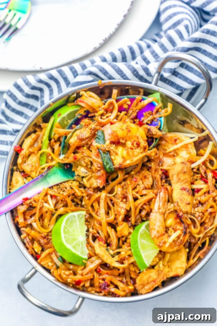 Effortless Chicken and Shrimp Pad Thai Noodles 2 A silver bowl filled with vibrant chicken and shrimp pad thai, garnished with fresh lime wedges and a spoon, ready to be enjoyed.