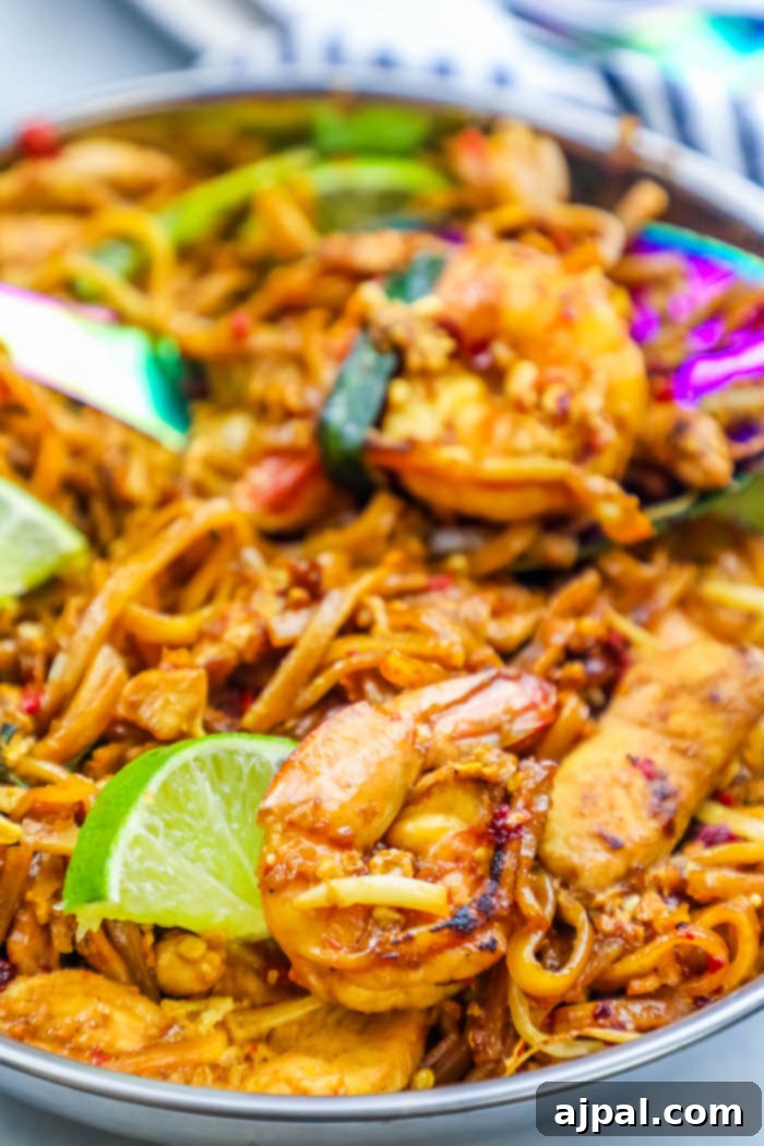 Effortless Chicken and Shrimp Pad Thai 4 A vibrant pan of Chicken and Shrimp Pad Thai Noodles, stir-fried to perfection with fresh lime wedges, showcasing an easy and delicious Thai dinner recipe.