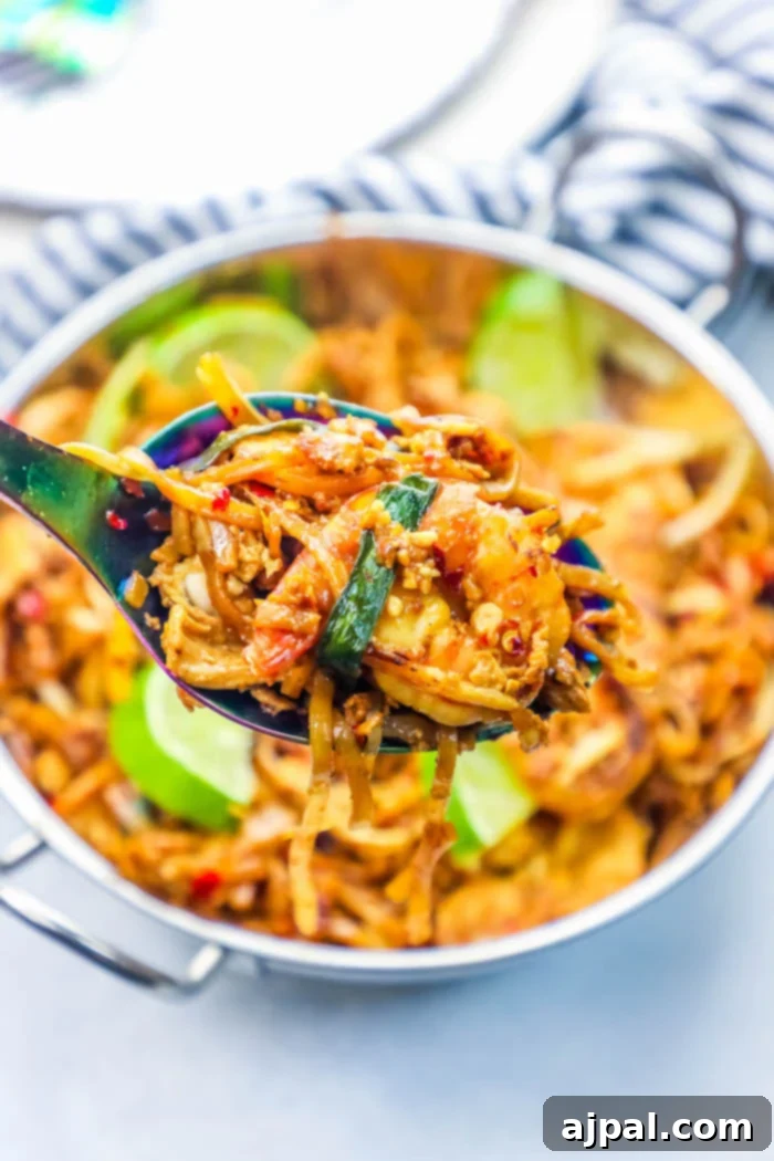Effortless Chicken and Shrimp Pad Thai Noodles 5 A spoonful of homemade chicken and shrimp pad thai, showcasing the rich sauce, perfectly cooked noodles, and colorful garnishes, ready to be savored.