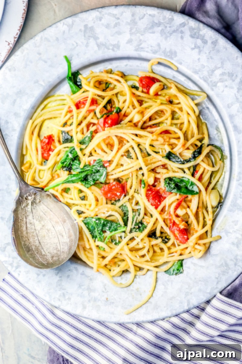 Garlic Butter Spinach Parmesan Spaghetti 2 A generous serving of Spinach Parmesan Garlic Butter Spaghetti, adorned with fresh tomatoes and parsley, showcasing its rich, creamy texture.