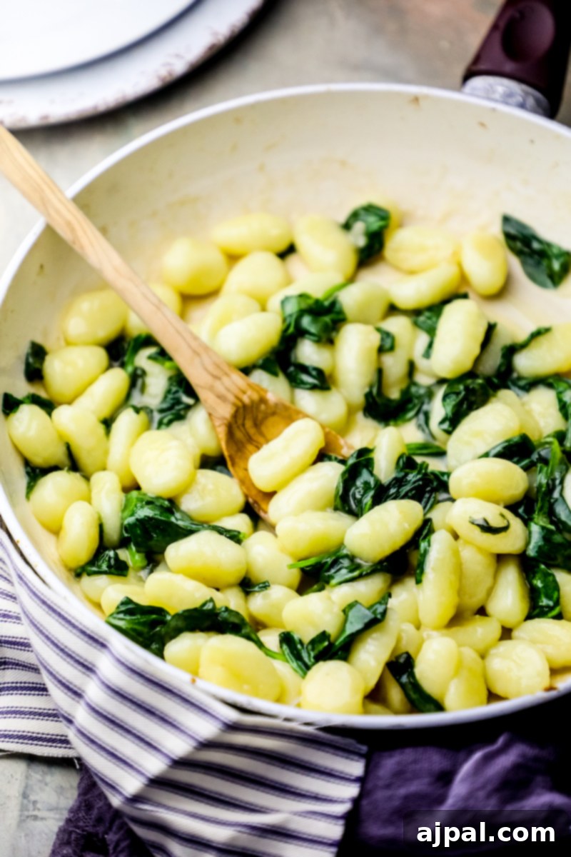 A pan filled with creamy spinach parmesan gnocchi, cooked to perfection, with a wooden spoon resting inside, ready for serving.