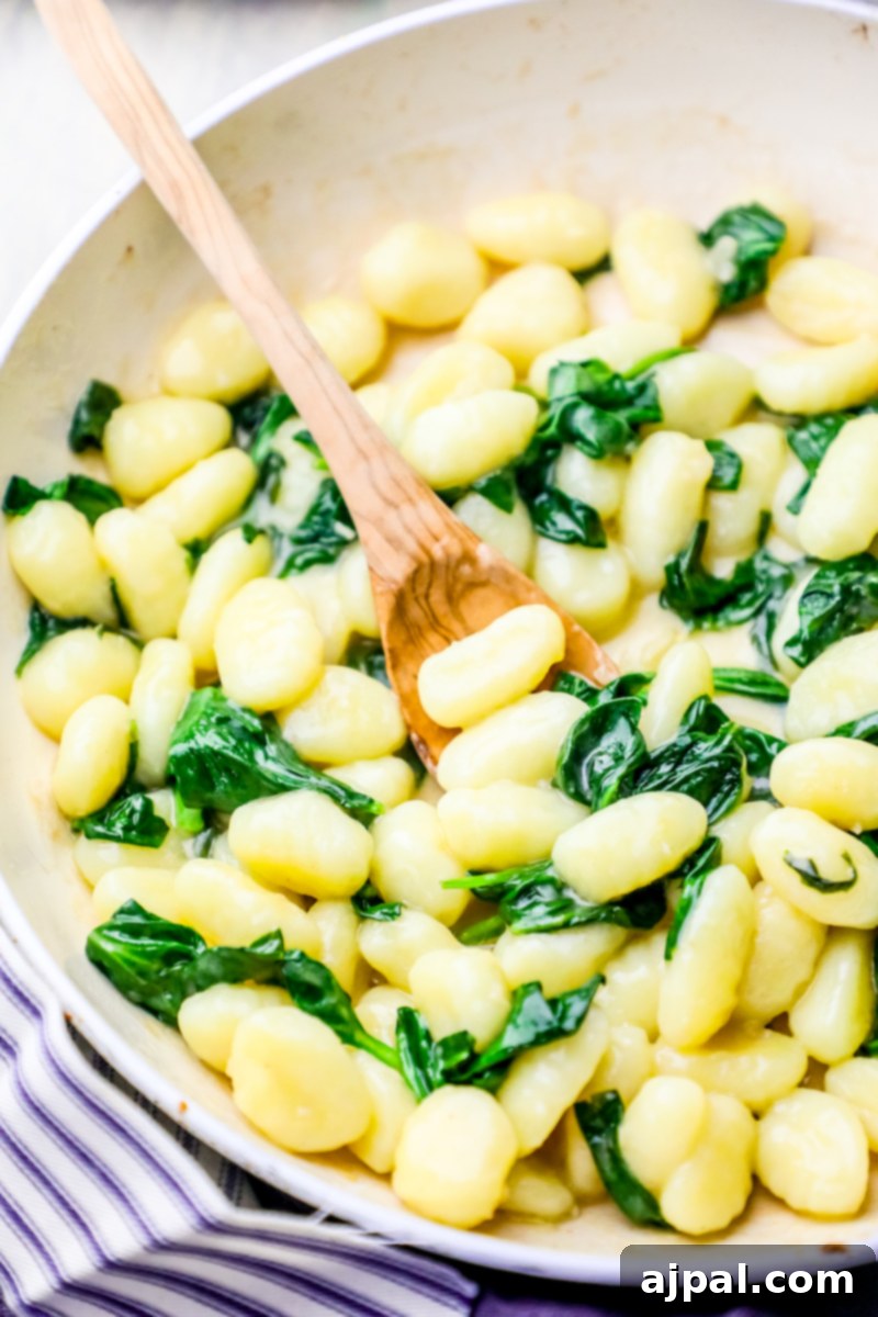 A close-up of creamy spinach parmesan gnocchi simmering in a pan with a wooden spoon, showcasing the rich texture and vibrant colors.