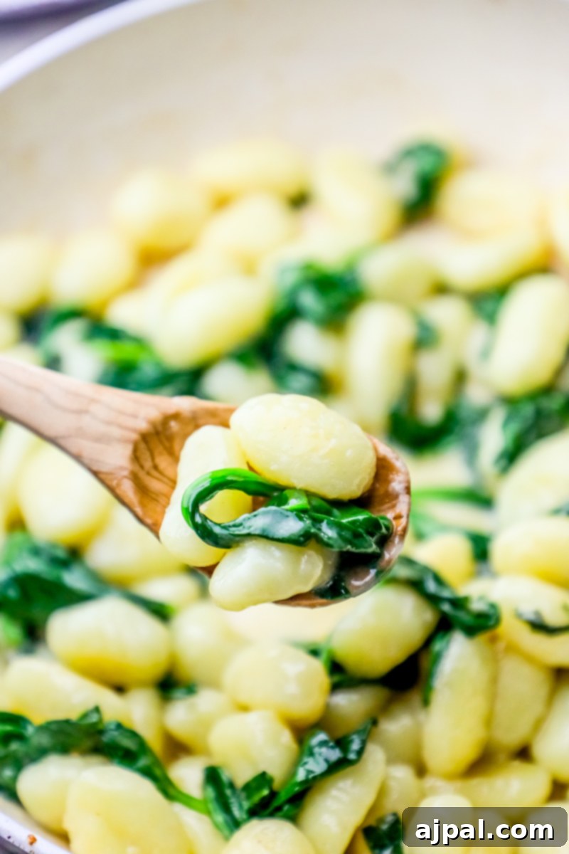 A wooden spoon serves creamy spinach parmesan gnocchi from a pan, highlighting the one-pot cooking method and delicious texture.