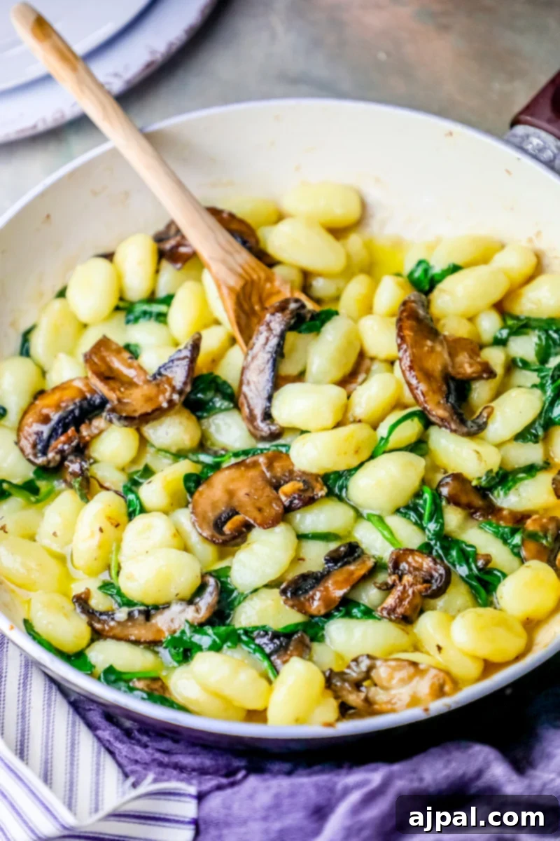 Mushrooms and spinach cooked with a wooden spoon in a pan.