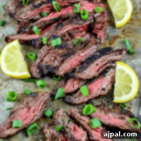 Sliced garlic grilled flank steak garnished with scallions and lemon wedges, all artfully arranged on a metal tray.