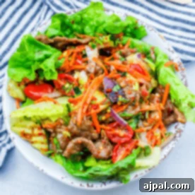 A vibrant beef salad with lettuce, carrots, cucumbers, tomatoes, and a spicy keto dressing, served in a white bowl.