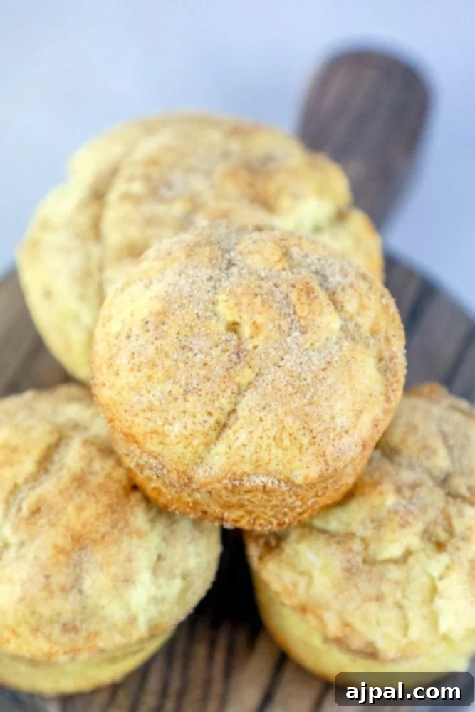 Piled high snickerdoodle muffins dusted with cinnamon sugar on a rustic cutting board, ready to be enjoyed.
