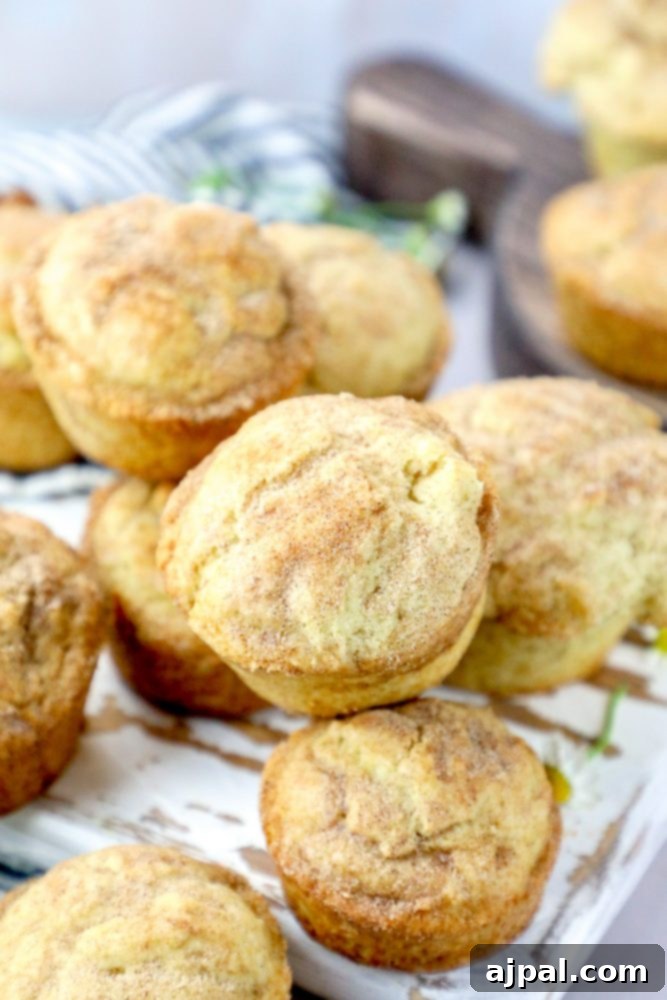 A close-up shot of several snickerdoodle muffins, beautifully browned and coated in sparkling cinnamon sugar, presented on a wooden board.