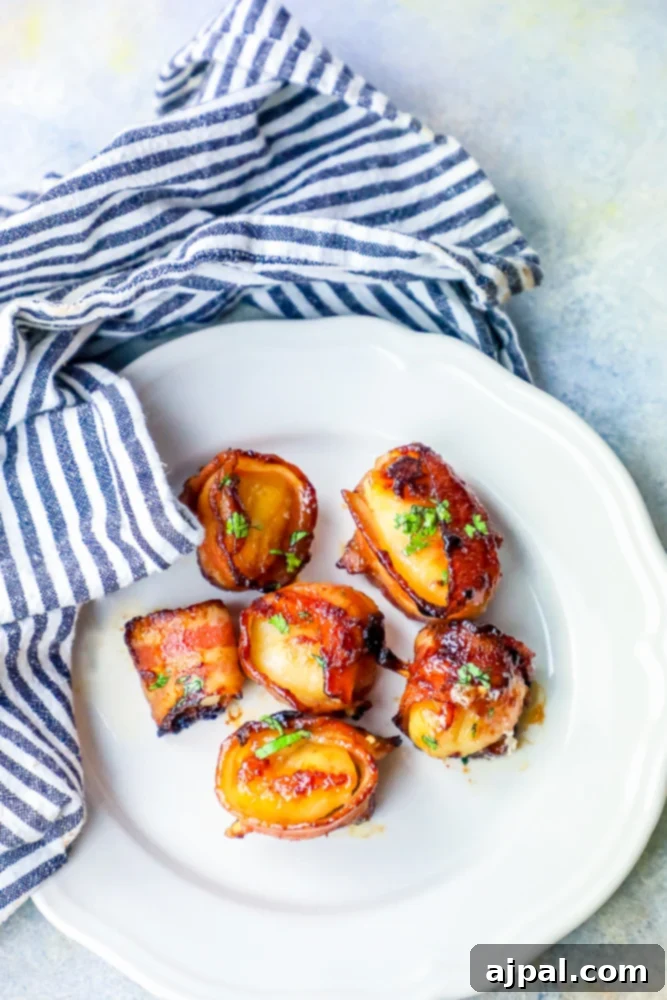 A serving of delectable bacon wrapped scallops with a glistening brown sugar glaze, presented beautifully on a plate with a crisp napkin in the background