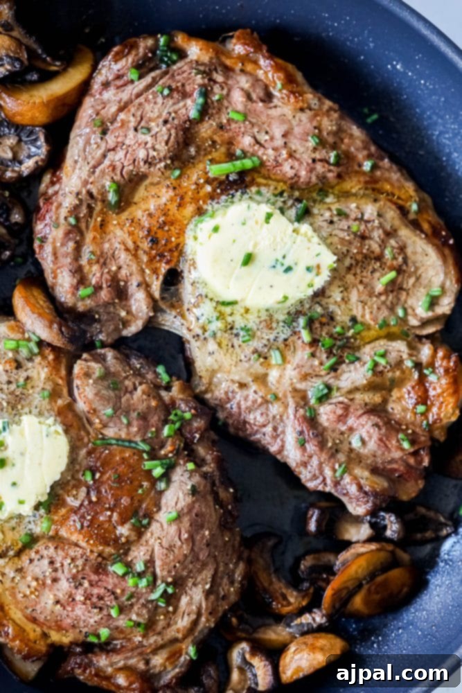 A perfectly cooked ribeye steak with a pat of garlic herb butter, nestled amongst sautéed mushrooms in a cast iron pan.