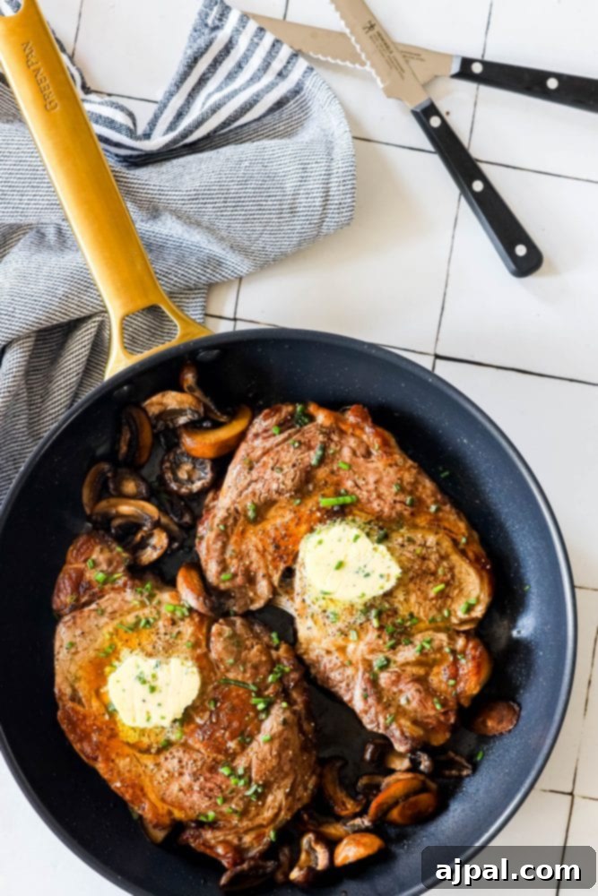 Close-up of golden-brown ribeye steaks in a pan with seasoned mushrooms, glistening with butter, ready to be served.
