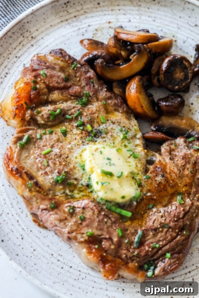 A perfectly broiled ribeye steak on a white plate, accompanied by savory mushrooms and a dollop of herb butter.