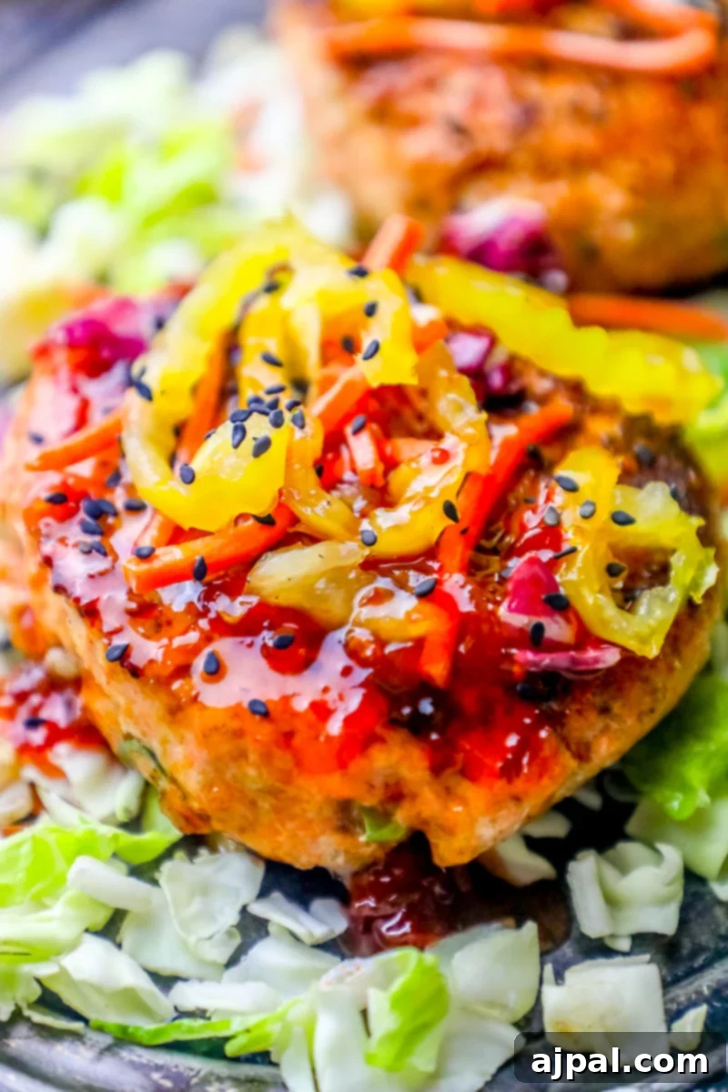Sweet Chili Glazed Asian Salmon Burgers 2 A beautifully grilled salmon patty, drizzled with sweet chili sauce, garnished with pepperoncini, and served on a crisp lettuce leaf, ready to be enjoyed.