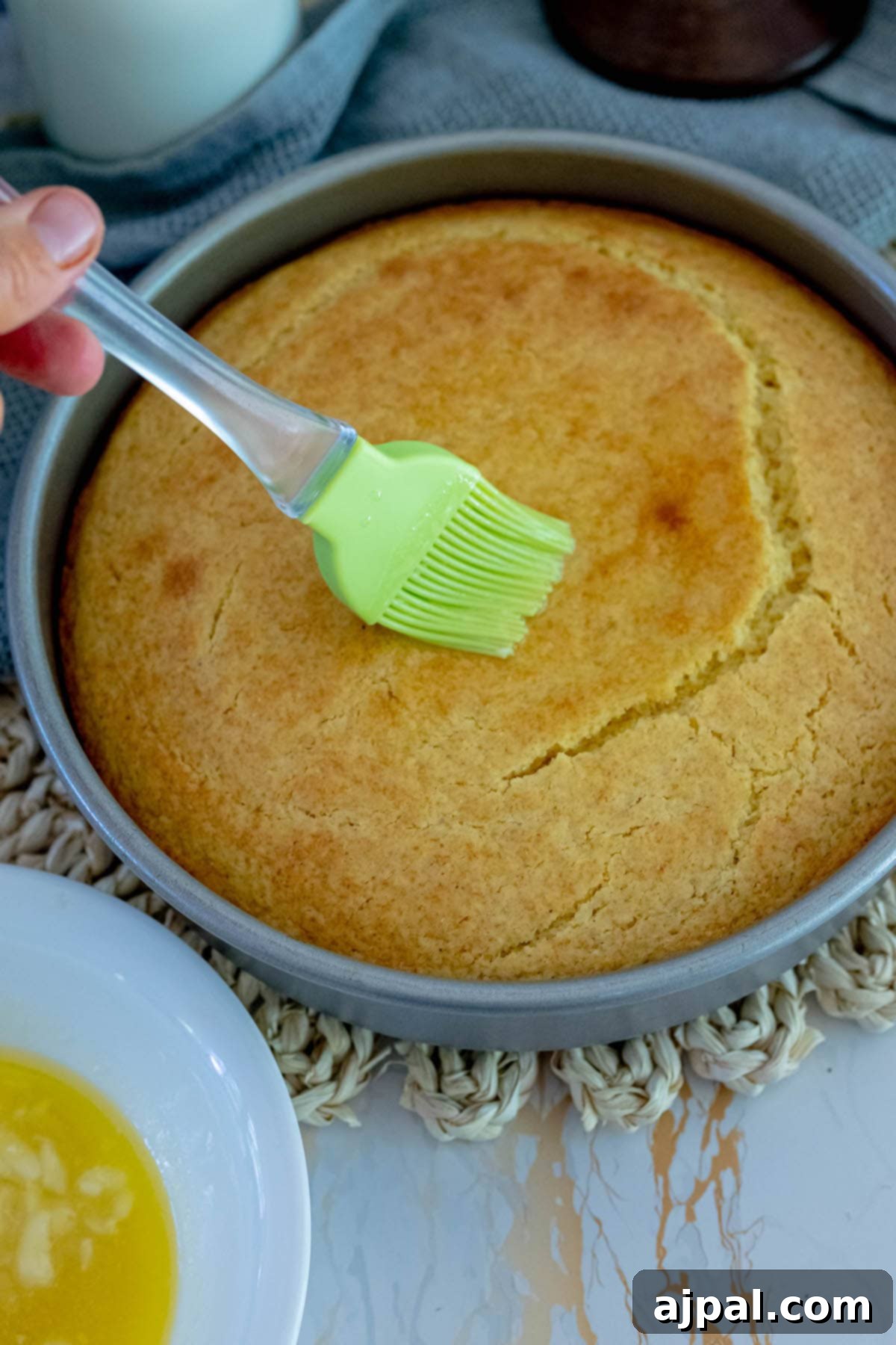Baked cornbread in a pan, with melted honey butter being brushed on top.