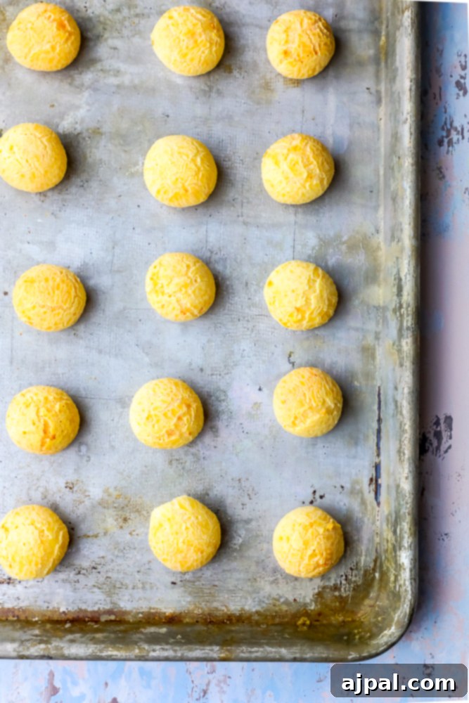 Easy Fogo De Chao Style Brazilian Cheese Bread 4 A baking sheet full of Brazilian cheese bread rolls on a blue background.