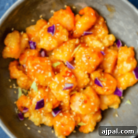 A bowl of breaded shrimp coated in an orange glaze, garnished with sesame seeds and small purple cabbage pieces, inspired by The Best Easy Bang Bang Shrimp Recipe - Bonefish Grill Copycat.