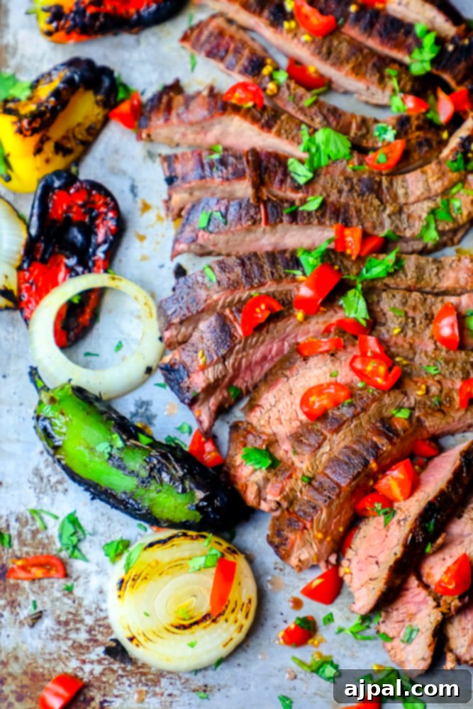 Ultimate Carne Asada 2 Tender, thinly sliced grilled carne asada steak resting on a platter, garnished with fresh chiles and charred bell peppers and onions in the background, ready to be served for a delicious meal.
