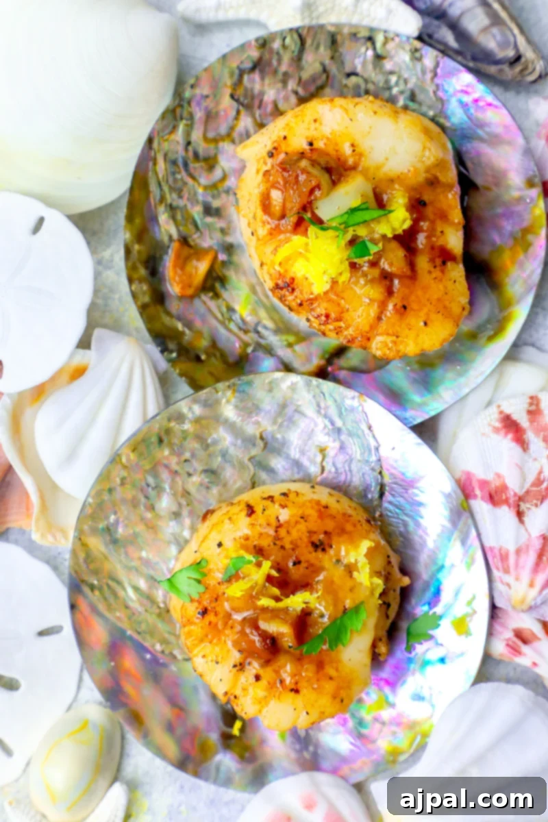 Two exquisite lemon garlic butter scallops artfully presented on a seashell plate.