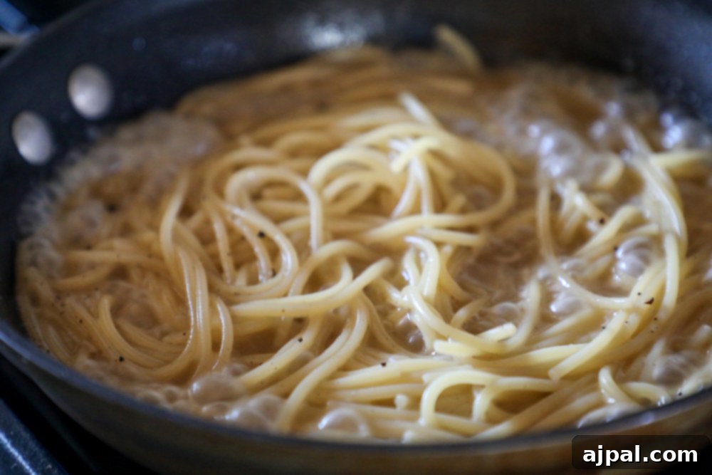 A close-up of Cacio e Pepe spaghetti in a frying pan, ready to be served, showcasing its creamy texture.
