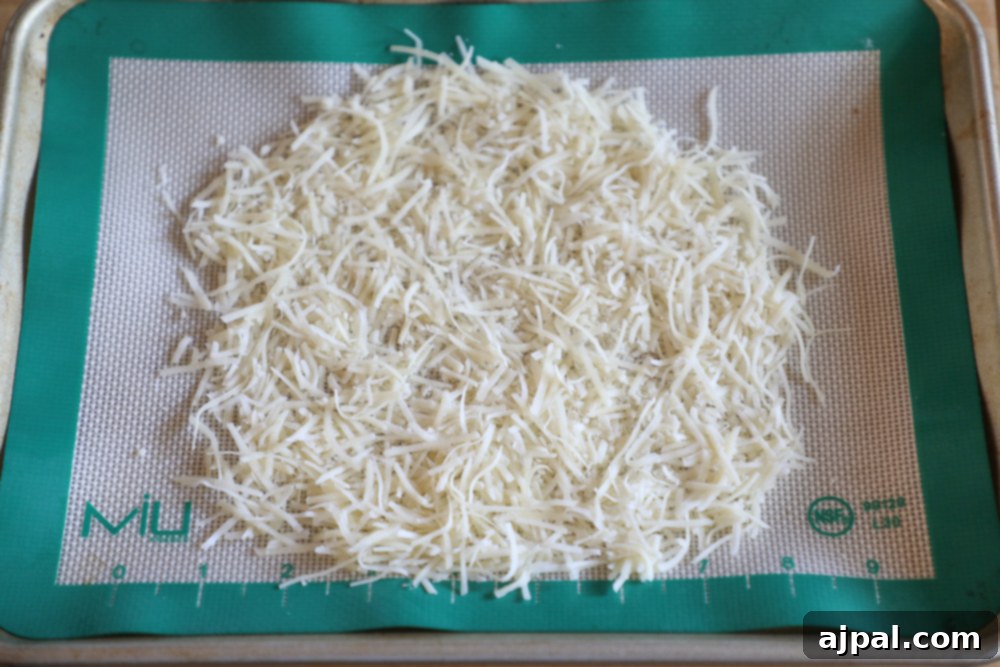 Shredded Parmesan cheese evenly spread on a baking sheet lined with a silicone mat, ready for baking into an edible bowl.