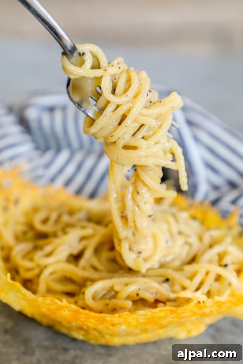 A fork lifts strands of creamy Cacio e Pepe pasta from an edible Parmesan bowl, showcasing the perfect texture and the delectable finished dish.