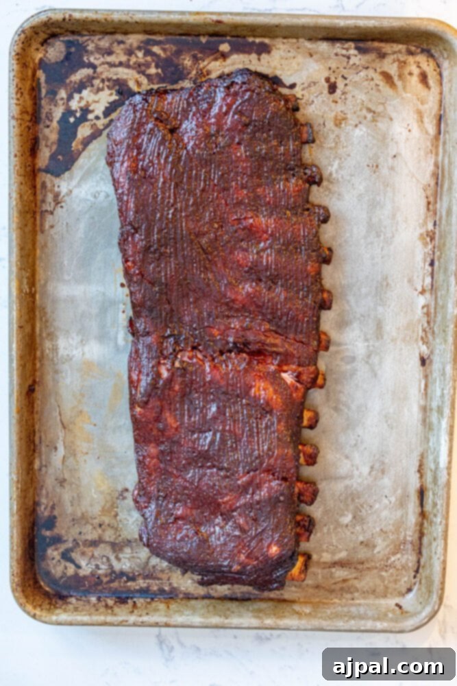A picture of sauced ribs glistening on a baking sheet, showcasing a delicious, caramelized BBQ glaze.