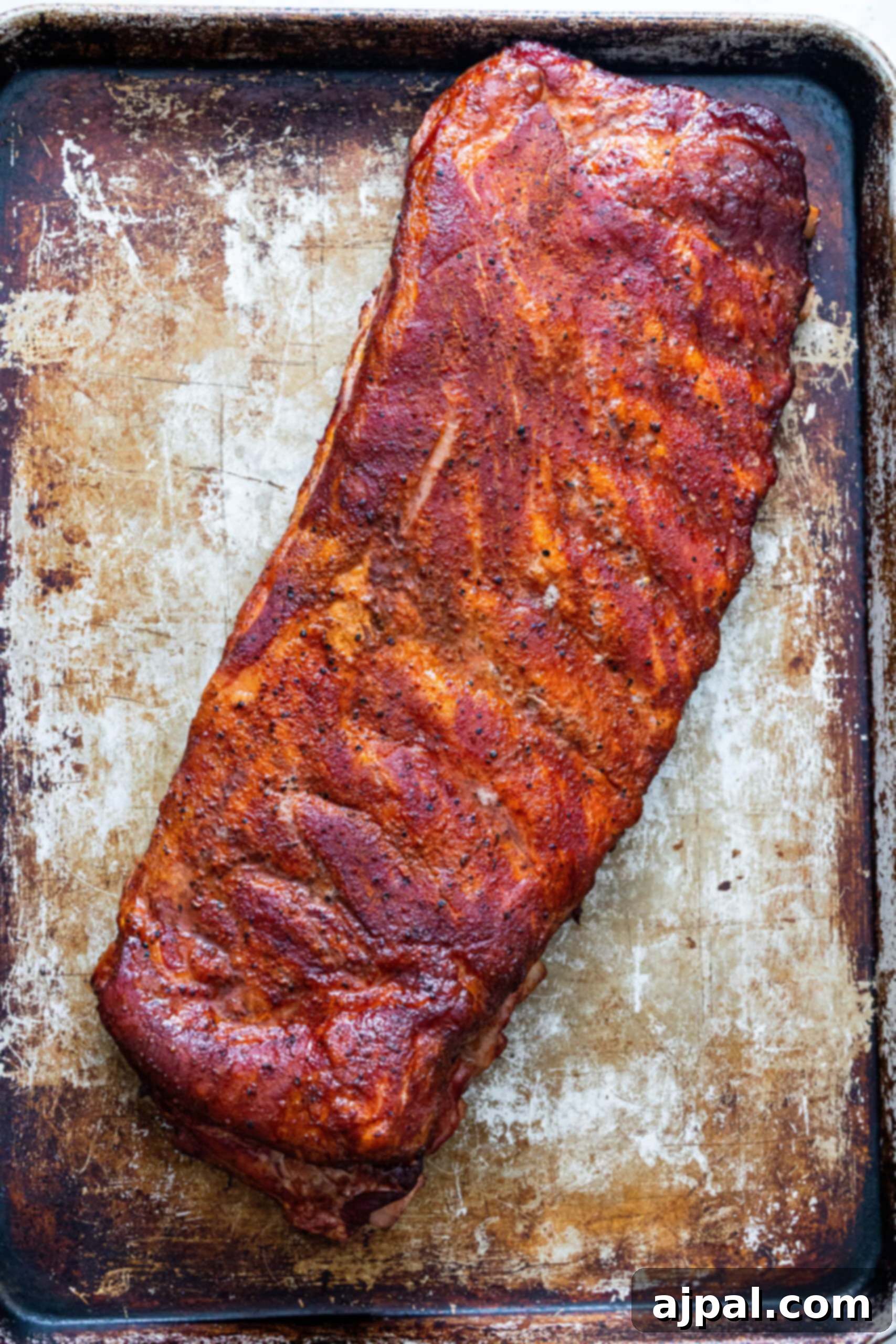 A rack of perfectly smoked ribs resting on a baking sheet, displaying a beautiful dark red color from the initial smoking phase.