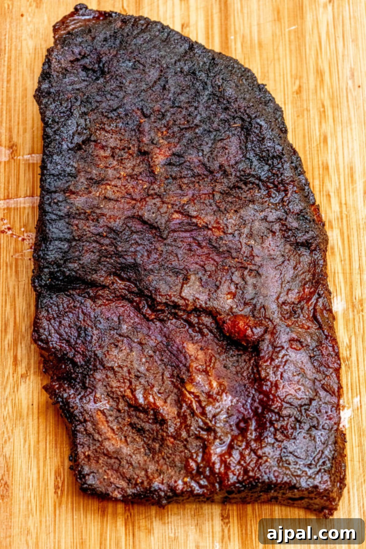 A large, beautifully smoked brisket, freshly removed from the grill, resting on a wooden cutting board.