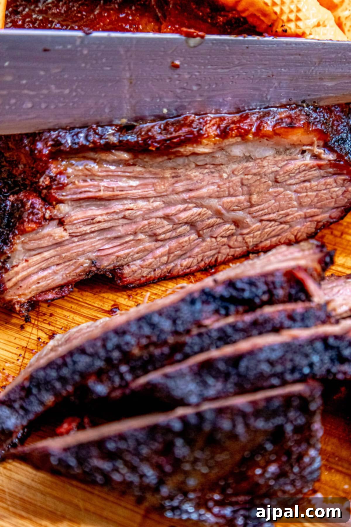 A skilled hand carving tender slices of smoked brisket with a sharp knife on a wooden board.