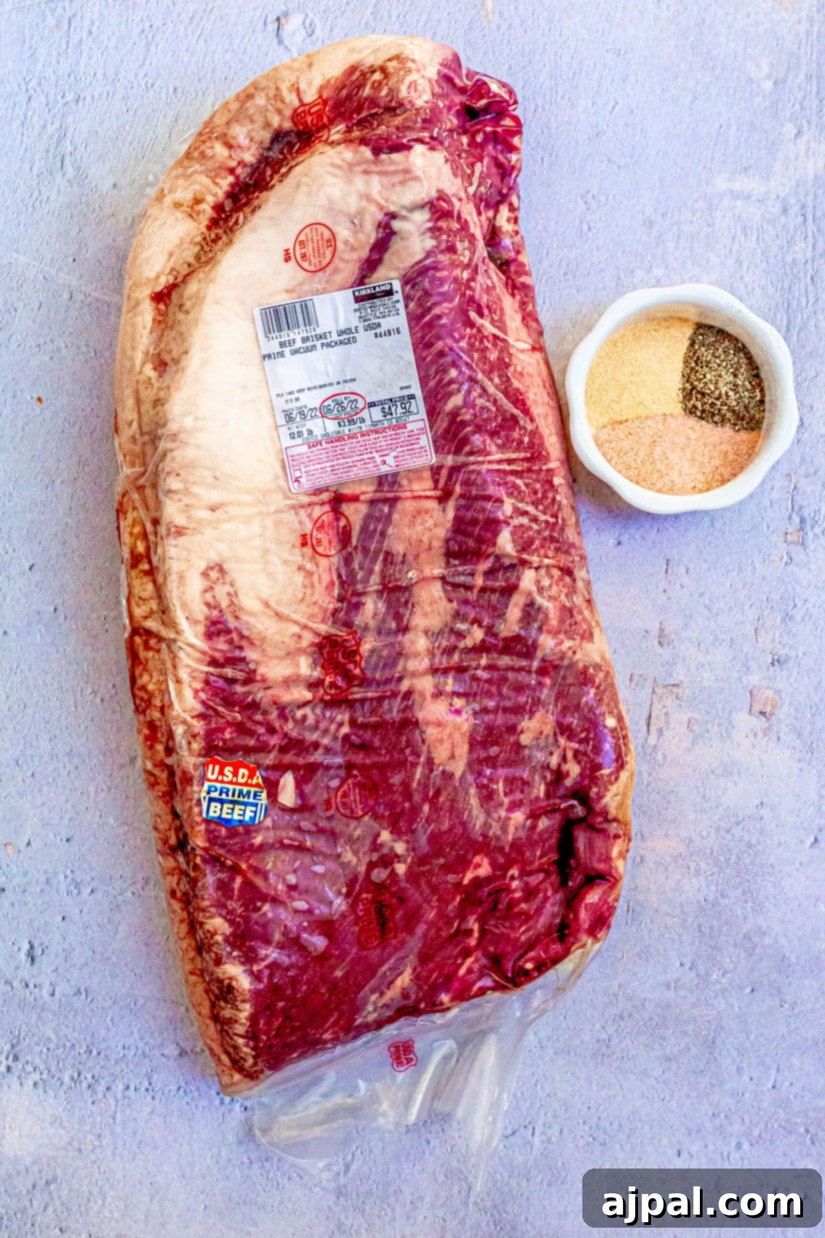 A raw, seasoned brisket, ready for the smoker, placed on a baking sheet with various spices nearby.