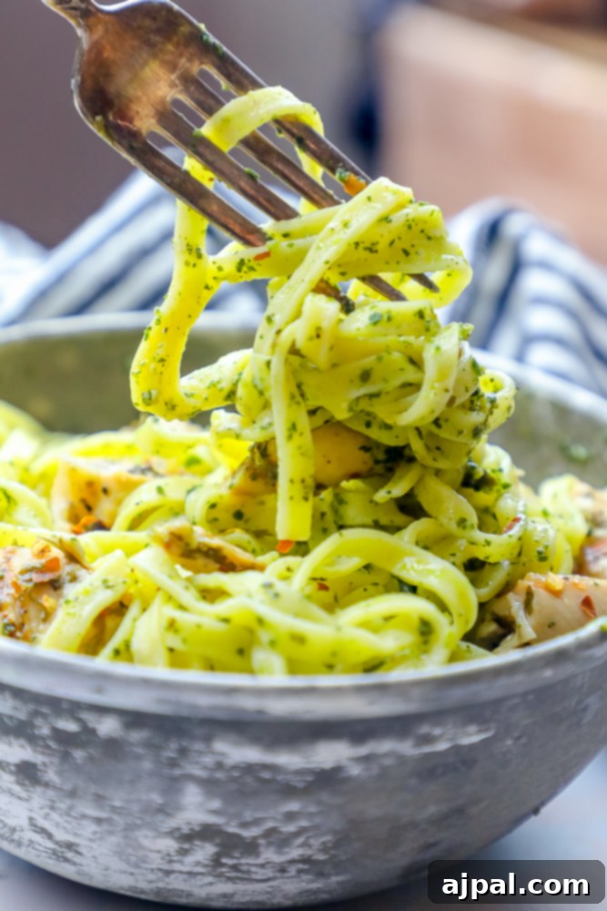 A beautifully presented bowl of chimichurri chicken pasta with a fork, showing the vibrant green sauce clinging to the pasta and chicken pieces.