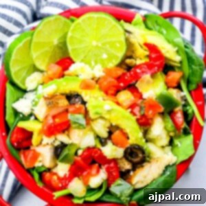 A red bowl filled with chicken, vegetables, and lime wedges, perfect for a keto chicken taco salad.