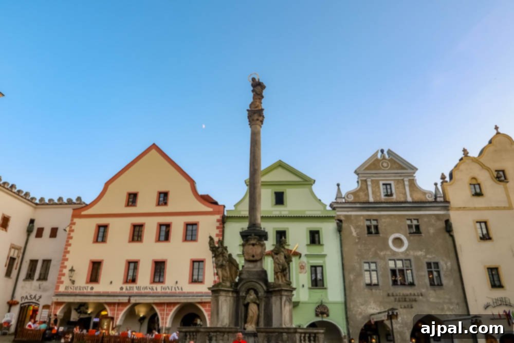 The charming town square of Cesky Krumlov at sunset, featuring a historic statue and colorful buildings bathed in warm light.