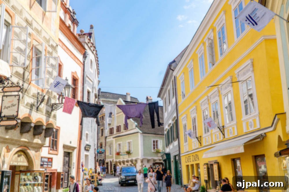 People strolling down a bustling cobblestone street in Cesky Krumlov's Old Town, with historic buildings and charming details like hanging laundry visible.