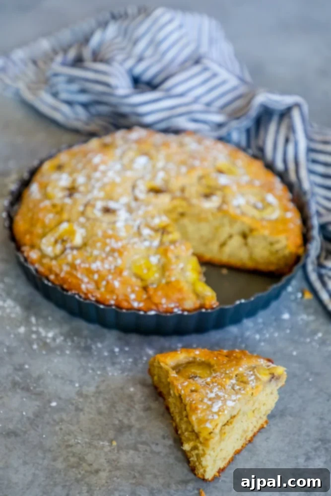 Effortless Apple Banana Loaf 2 A golden-brown slice of apple banana cake bread resting on a rustic wooden table, next to a blue tablecloth, hinting at a cozy breakfast or delicious snack.