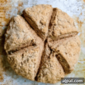 A round loaf of golden-brown whole-grain soda bread, traditionally cut into six triangular pieces on a baking tray.