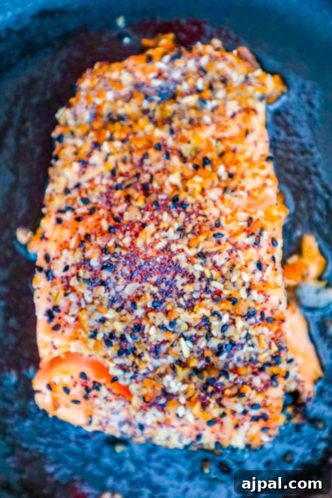 A glistening salmon fillet, fresh from the oven, adorned with a golden-brown everything bagel crust.