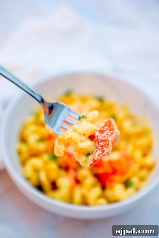 A fork lifting a delicious bite of lobster mac and cheese from a white bowl.