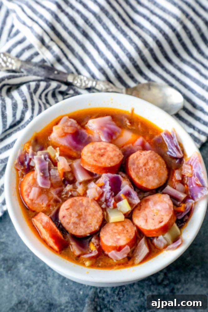 A hearty bowl of sausage and cabbage soup dolloped with a spoon.