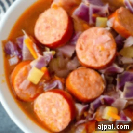 A bowl of savory sausage and red cabbage, accompanied by chopped vegetables, immersed in a rich broth—an easy cabbage and sausage soup perfect for those seeking a delicious keto-friendly option.